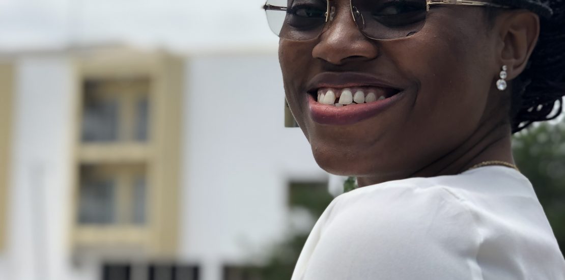 An image of Jane OLUWADARE wearing a white blouse and glasses and smiling into the camera